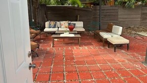 An outdoor patio area with a brick floor, a wooden table, and several white cushioned chairs. - Charming secure 2 bedroom home near Miami AirPort. Free parking (Miami)