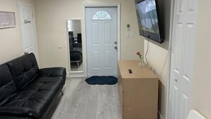 A room with a black leather sofa, a wooden cabinet, a television mounted on the wall, and a white door. - Charming secure 2 bedroom home near Miami AirPort. Free parking (Miami)