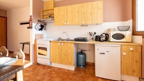 A compact kitchen with wooden cabinets, a gas stove, a microwave, and a dishwasher. - Le p'tit Schuss (La Giettaz)
