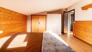 A bedroom with wooden paneling, a bed, a wardrobe, and a door leading to another room. - Le p'tit Schuss (La Giettaz)