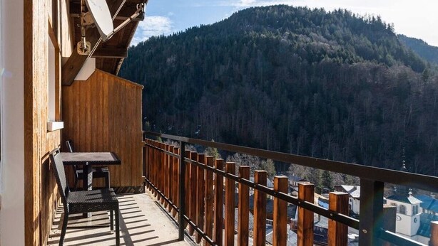 A wooden balcony with a table and chairs, overlooking a forested mountain. - Le p'tit Schuss (La Giettaz)