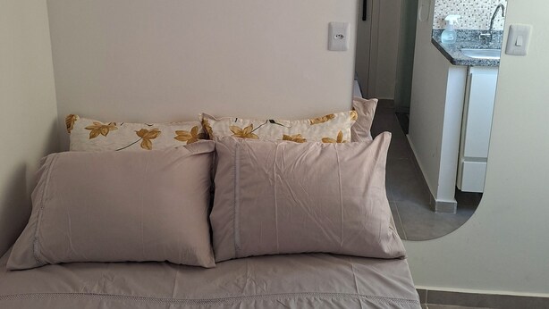 Een slaapkamer met een bed, kussens en uitzicht op de keuken.