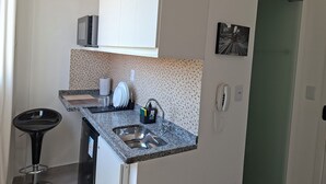 Een kleine keuken met een granieten aanrecht, een roestvrijstalen spoelbak en een barstoel.