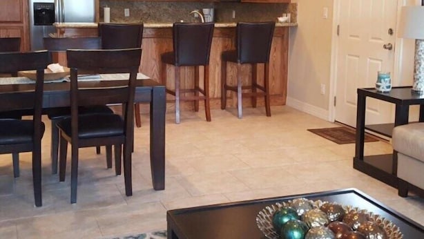 Una cocina moderna con armarios de madera, un refrigerador y lámparas colgantes. Hay una zona de comedor con una mesa y sillas, y una mesa de centro con objetos decorativos.
