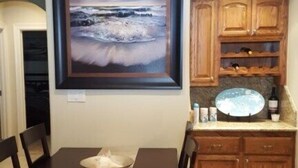 Un comedor con mesa y sillas, una cocina con armarios de madera y un cuadro enmarcado en la pared.