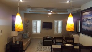 Una sala de estar con sofá, mesa de centro, sillas, un televisor de pantalla plana y dos lámparas colgantes.
