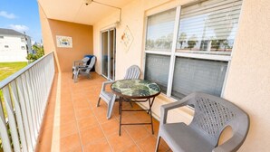 A balcony with a table and two chairs, a window with blinds, and a door. - Two Bedroom One Bath Off The Beach (South Padre Island)