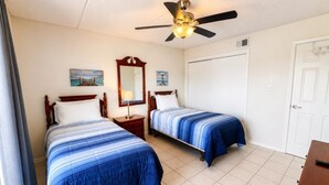 A hotel room with two beds, a ceiling fan, a large mirror, and a door. - Two Bedroom One Bath Off The Beach (South Padre Island)