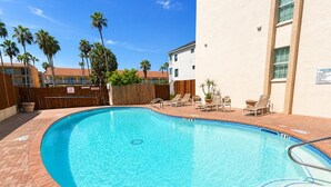 A swimming pool with a brick border, surrounded by lounge chairs and a wooden fence. - Two Bedroom One Bath Off The Beach (South Padre Island)
