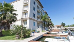 A multi-story hotel with balconies, a swimming pool, and palm trees. - Two Bedroom Two Bath Bayside Condo (South Padre Island)