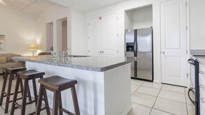 A modern kitchen with a central island, bar stools, a refrigerator, and a dishwasher. - Two Bedroom Two Bath Bayside Condo (South Padre Island)