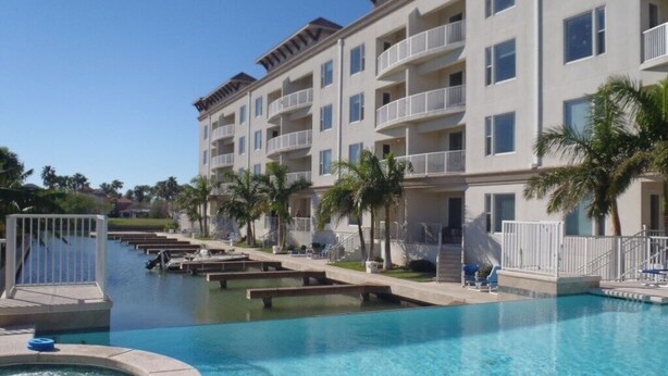 A hotel with a swimming pool, multiple balconies, and palm trees. - Two Bedroom Two Bath Bayside Condo (South Padre Island)
