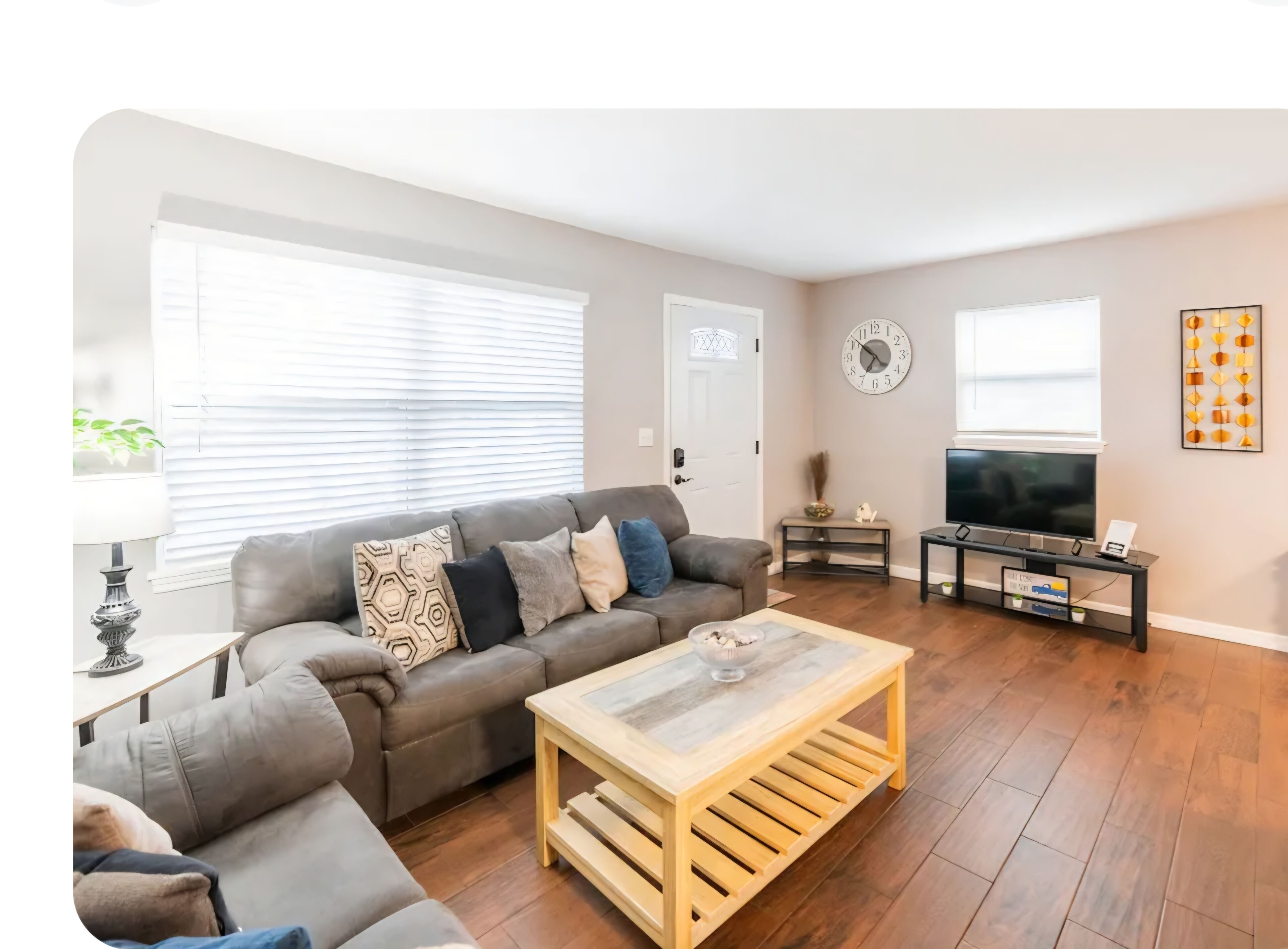 A living room with a sofa, coffee table, TV, and a clock on the wall.