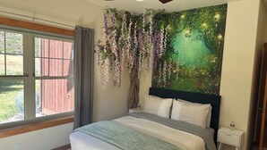Ein Schlafzimmer mit Bett, Nachttisch, Fenster und Deckenventilator, sowie Wandmalerei.