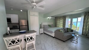 A modern hotel room with a kitchenette, a bed with a view, a dining area, and a balcony. - Beach Condo (St. John's)