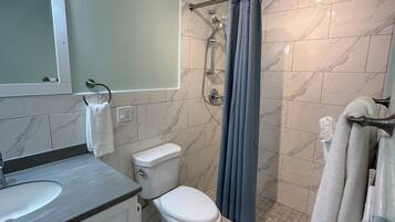 A bathroom with a toilet, sink, mirror, shower, and towel rack.