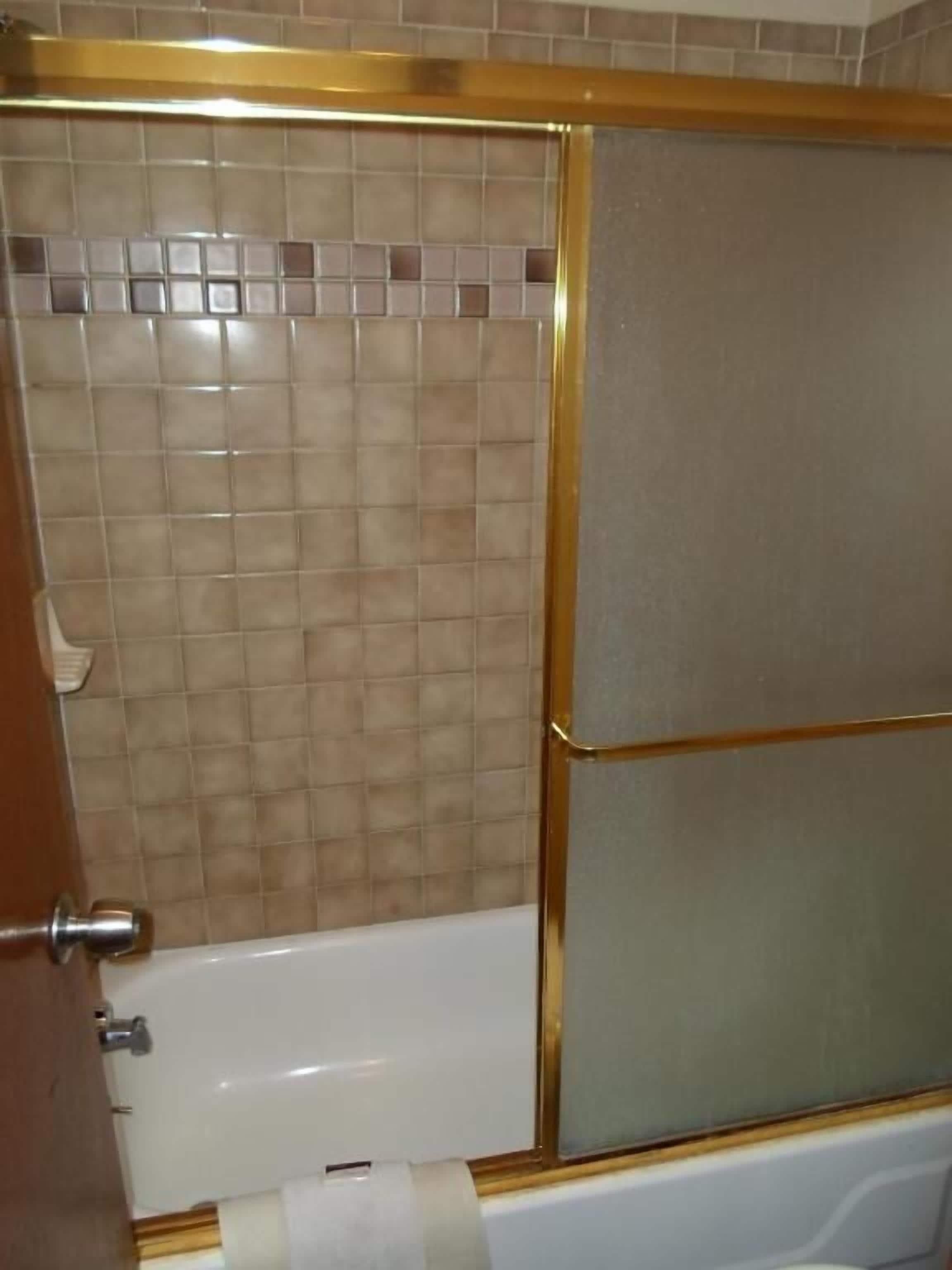 A bathroom with a bathtub, a shower enclosure, and a tiled wall.