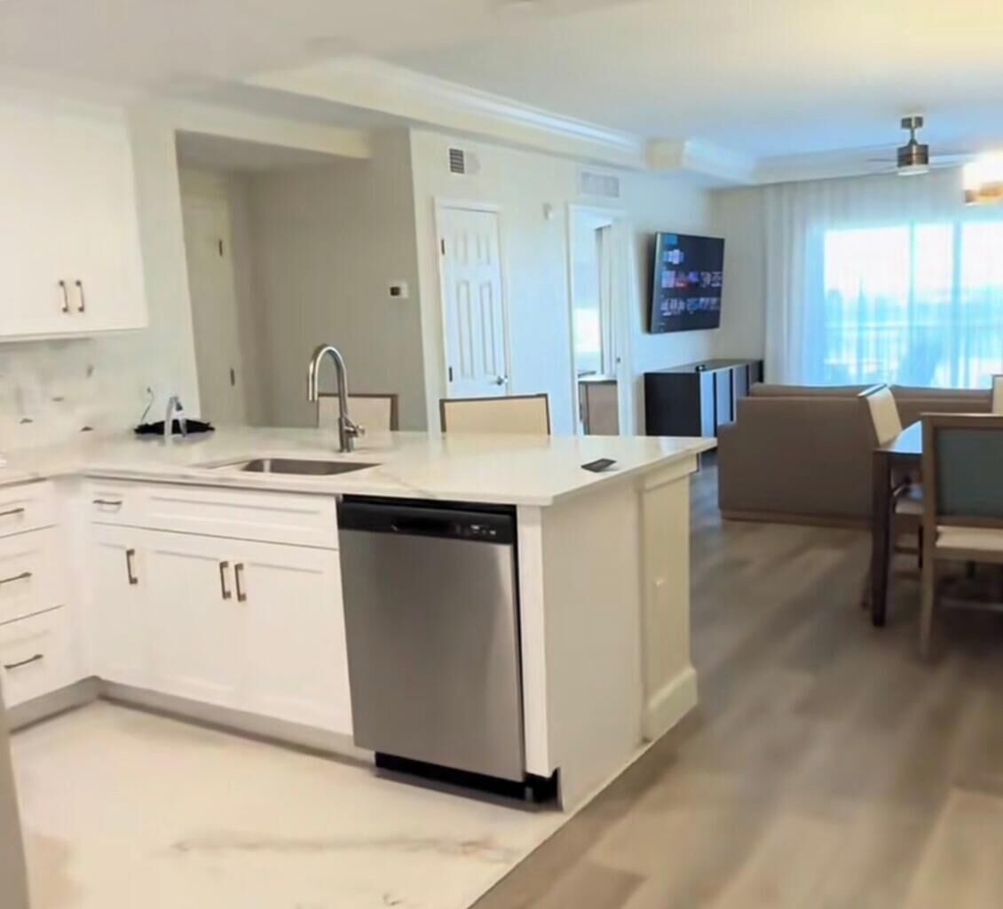 A modern kitchen with white cabinetry, a dishwasher, and a dining area with a table and chairs.