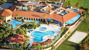 Un resort con múltiples piscinas, cancha de tenis y una amplia zona cubierta.