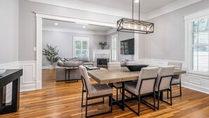 A spacious dining area with a wooden table and chairs, a modern chandelier, and a cozy seating area with a fireplace.