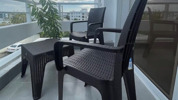 Ein Balkon mit zwei Korbstühlen, einem kleinen Tisch, einer Topfpflanze und Blick auf die Stadt.