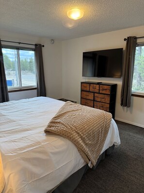 Une chambre à coucher avec un lit, un téléviseur fixé au mur et une commode.