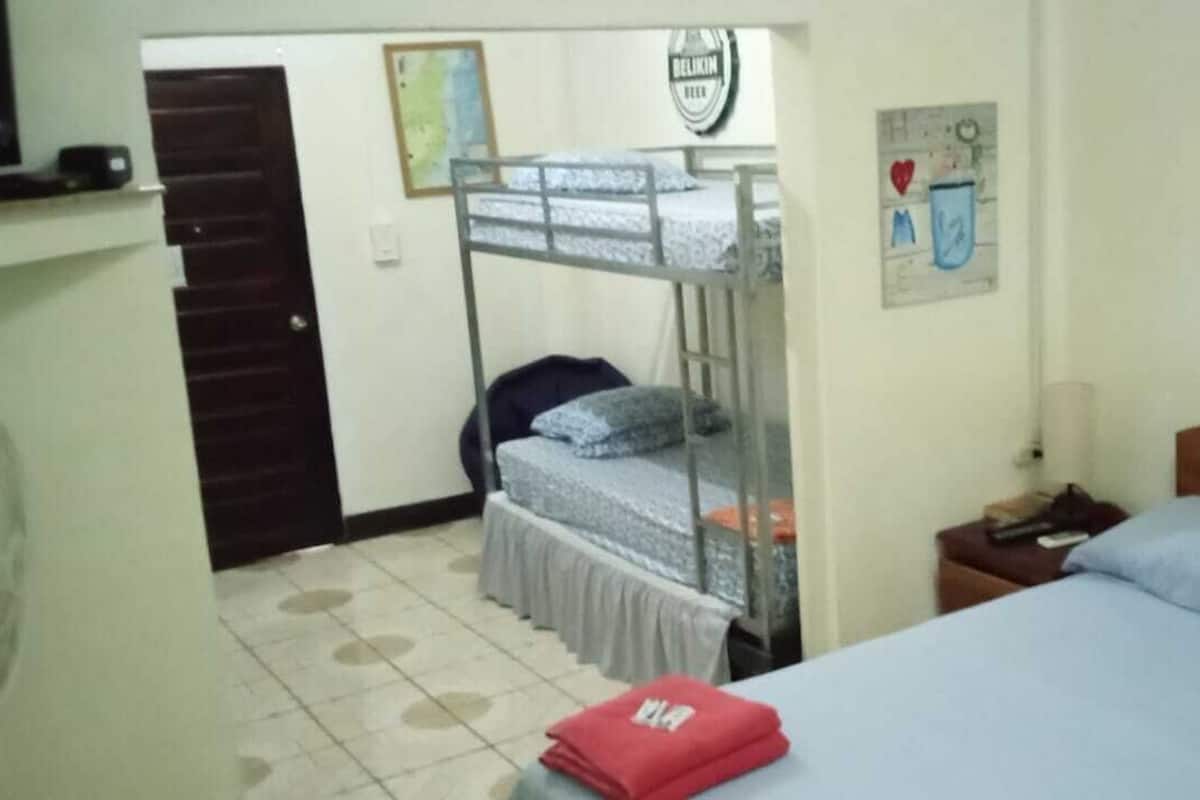 A bedroom with a bunk bed, a single bed, a nightstand with a lamp, and a wall with a tapestry.