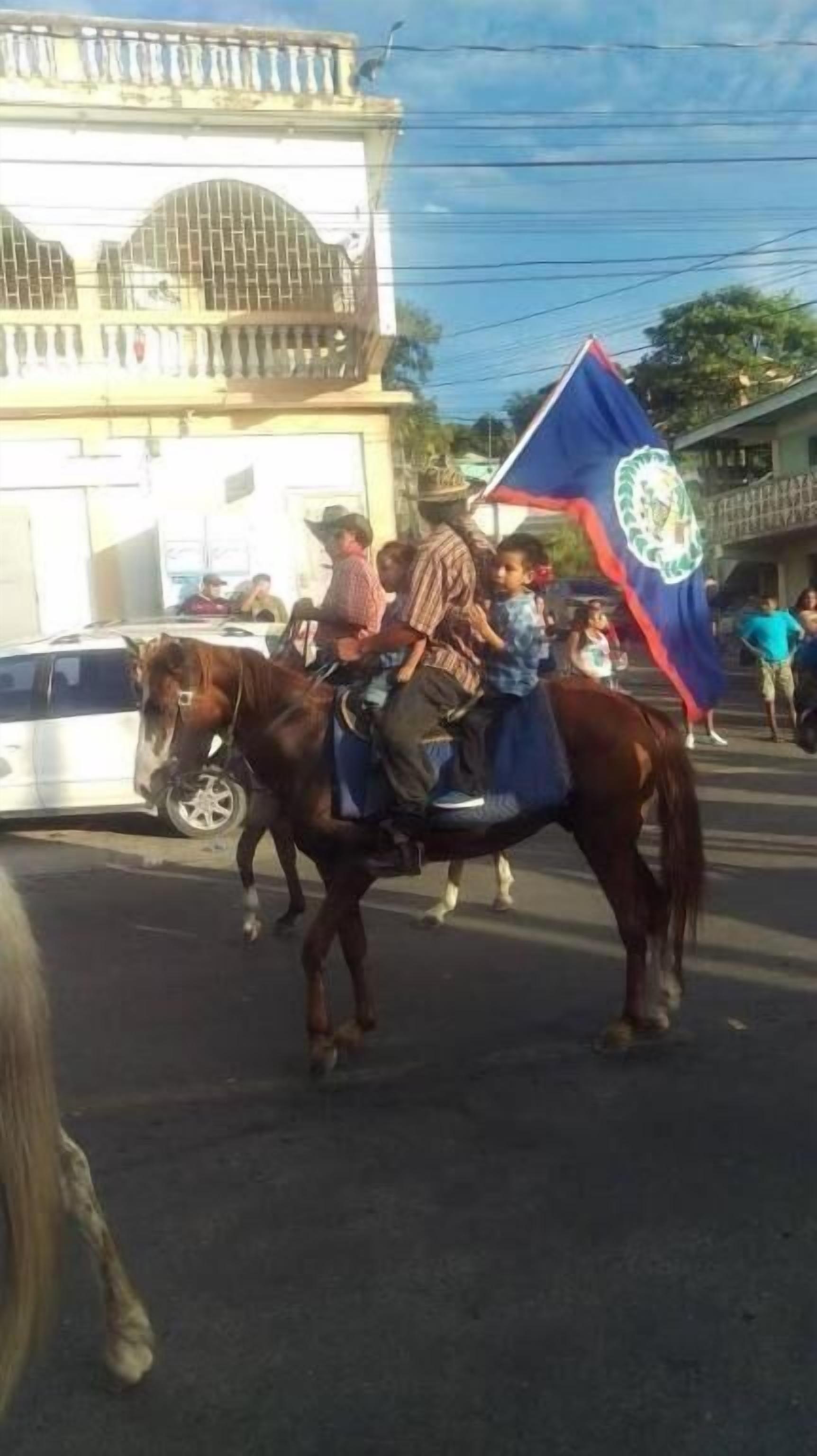 A horse-drawn carriage with passengers and a flag on a street.