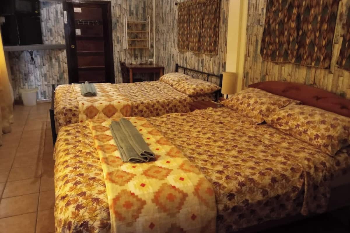 A hotel room with two beds, a wooden door, a small table, and a wall-mounted shelf.