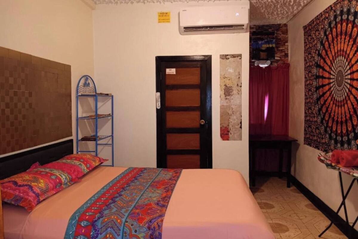 A hotel room with a bed, a shelf, a door, and a tapestry.