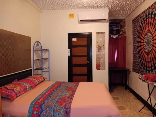 A hotel room with a bed, a shelf, a door, and a tapestry. - MAXROOMZ (Santa Elena)