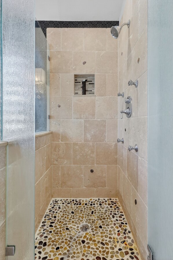 Una ducha con azulejos color beige y suelo de mosaico.