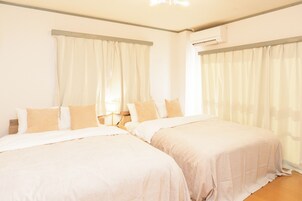 Habitación de hotel con dos camas, ropa de cama blanca, almohadas color beige y piso de madera.