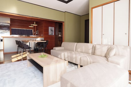 A modern living room with a beige sectional sofa, a wooden coffee table, and a dining area with chairs and a table.