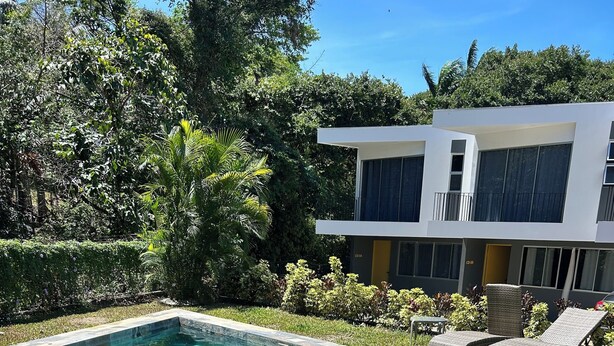 A rectangular pool with clear blue water, surrounded by a stone border and grass. There are two wicker lounge chairs and a small table near the pool. - Great townhome with AC in Guácima, surrounded with nature and totally private (Guácima)