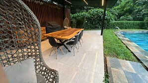 An outdoor patio with a wooden table and chairs, a wicker chair, and a pool. - Great townhome with AC in Guácima, surrounded with nature and totally private (Guácima)