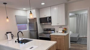 Una cocina moderna con armarios blancos, electrodomésticos de acero inoxidable, encimera de mármol e iluminación colgante.