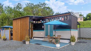 A small, single-story building with a covered patio area, a wooden deck, and a blue umbrella.