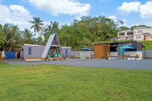 A modern building with a sloped roof, a covered outdoor seating area, and a small garden. - Rustic cabin container with AC in charming Manatí for relaxing days (Manatí)