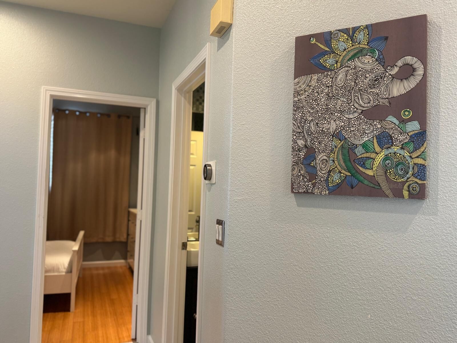 A hallway with a door leading to a room with a bed and a chair.