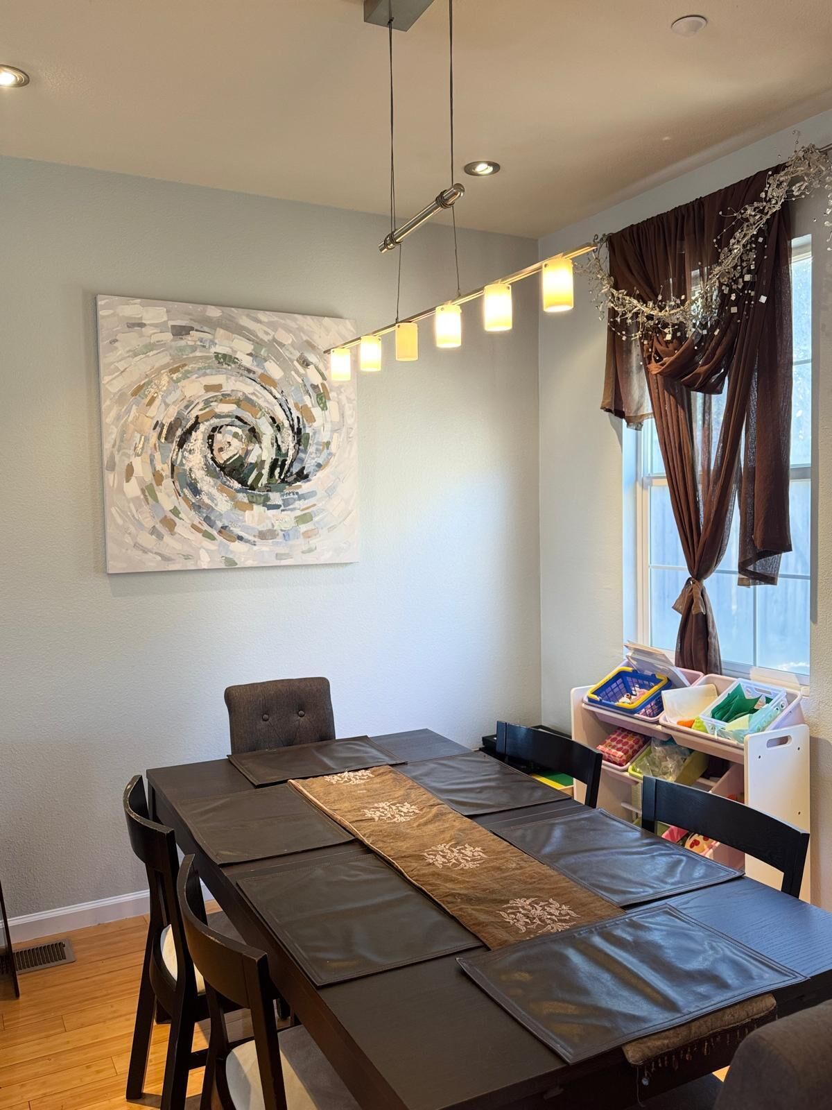 Un área de comedor con una mesa larga, sillas, un tapete decorativo y un cuadro abstracto colgado en la pared.