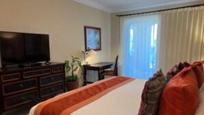 Habitació d'hotel amb llit, televisió, escriptori i finestra amb cortines.