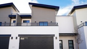 Un immeuble résidentiel moderne à deux étages, doté d’un garage, d’un balcon et d’un petit arbre dans le jardin avant.