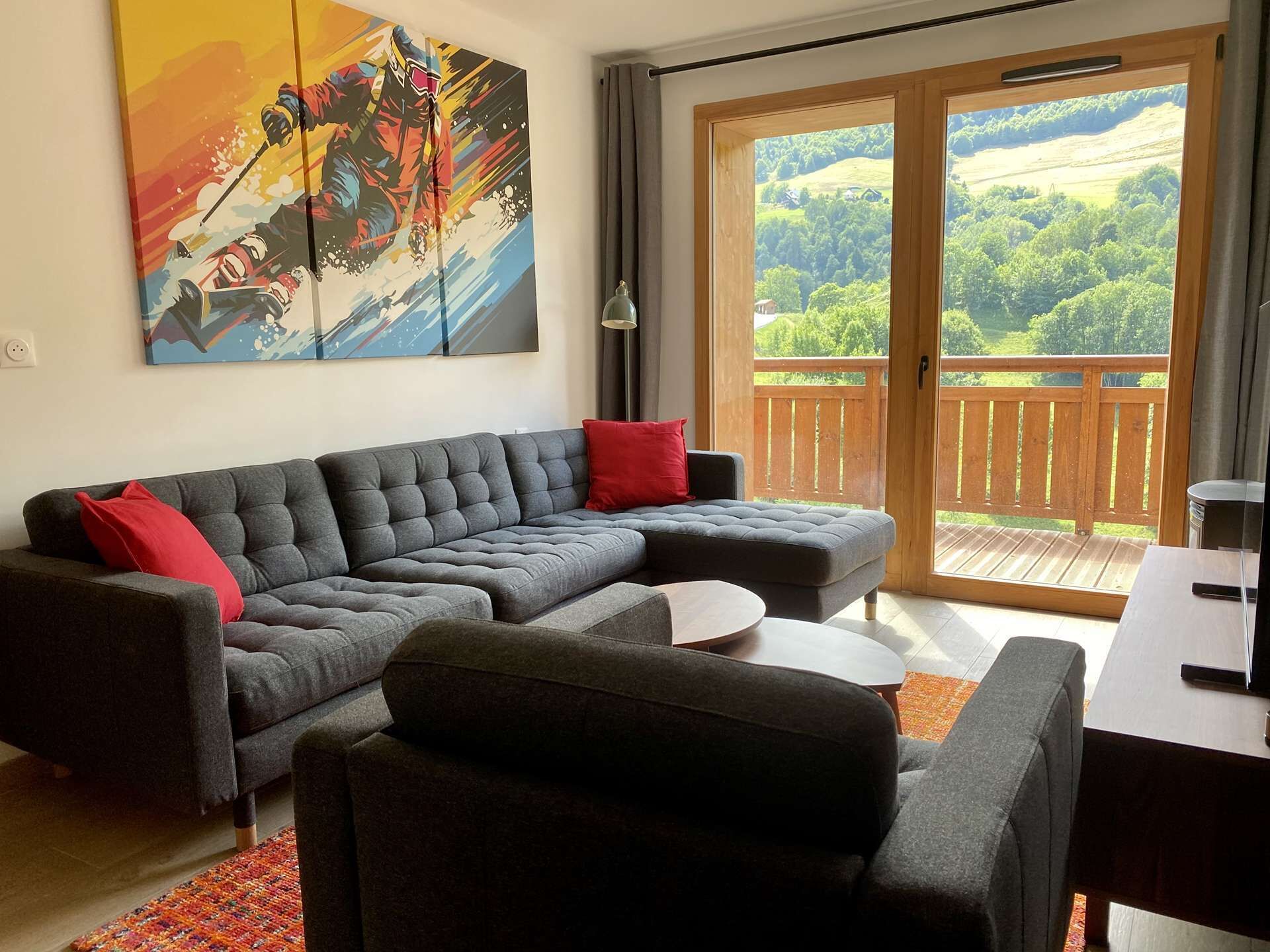 A modern living room with a grey sectional sofa, red cushions, a small white table, and a painting of a skier.