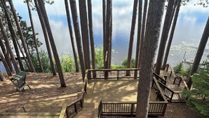 Une terrasse en bois, dotée de rampes de protection, qui offre une vue sur un lac et est entourée d’arbres.