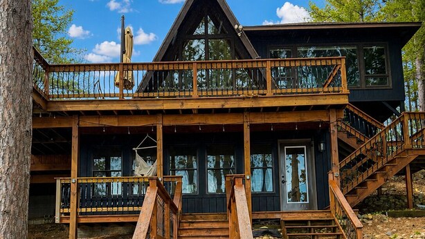 Une cabane avec un escalier en bois menant à une terrasse, le tout entouré d’arbres.