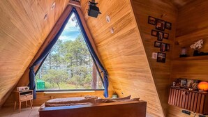 A cozy attic bedroom with a sloped ceiling, a large bed, a small desk, and a window offering a view of trees.