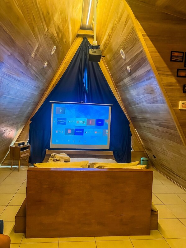 Une chambre confortable située sous les toits, avec un plafond en pente, un lit et un grand écran de télévision diffusant des services de streaming.