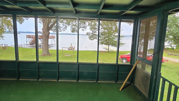 A covered outdoor area with a view of a lake, green artificial turf, and a wooden deck. - “Waterfront Getaway on Wheeler Lake – Private Dock & Boat Ramp” (Hillsboro)