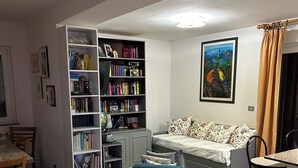 Un salon comprenant une bibliothèque, un canapé, un pouf bleu et un coin repas avec des chaises.